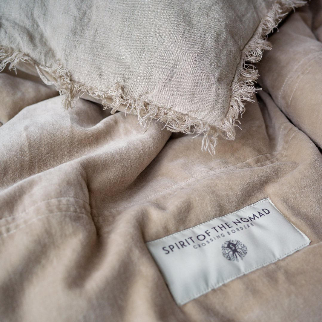 Close up of a Spirit of the Nomad beautiful bedspread. It shows the velvet side and the linen side along with the label detail.